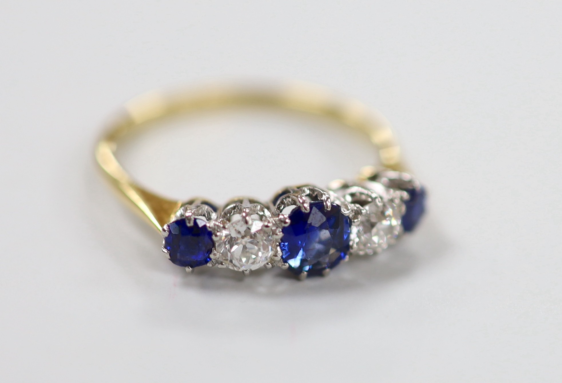 An 18ct, three stone sapphire and two stone diamond set half hoop ring, size P, gross weight 2.7 grams.